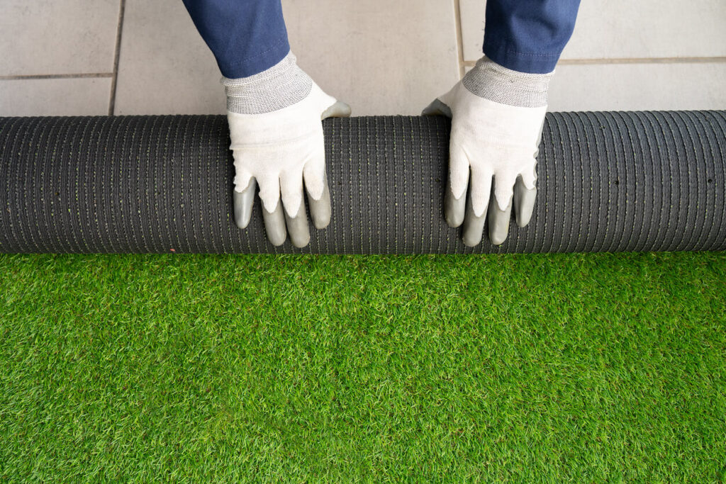 Men's hands holding a roll of artificial grass and installing it on a house.