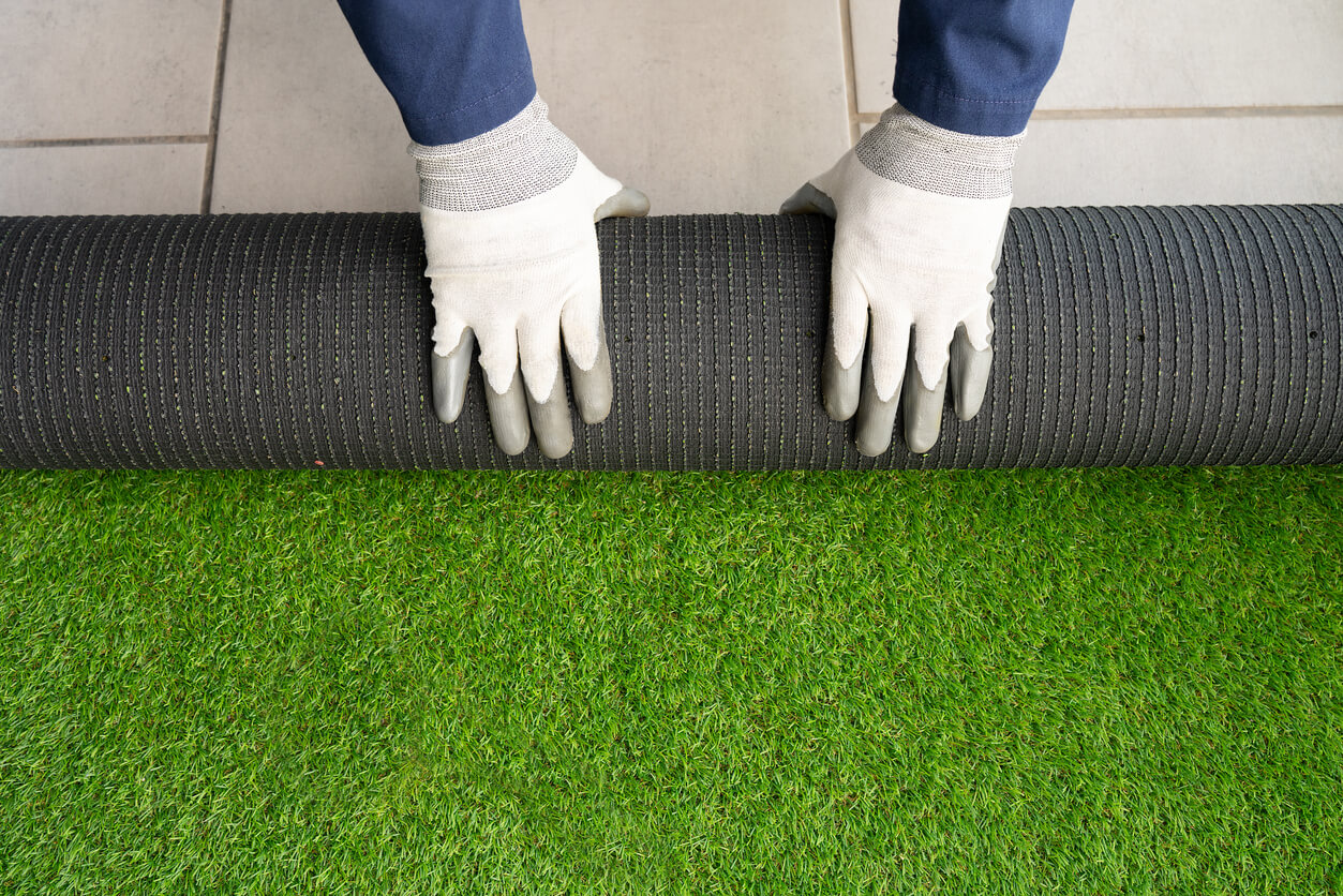 Men's hands holding a roll of artificial grass and installing it on a house.